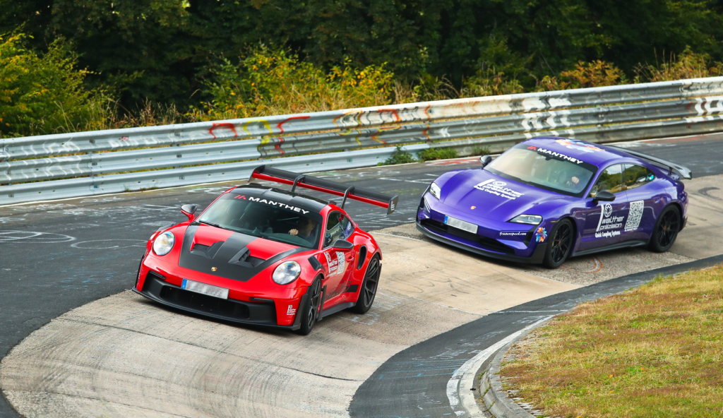 Zwei Rennsportwagen bei einem Motorsportrennen auf einer Kurvenstrecke inmitten grüner Landschaft